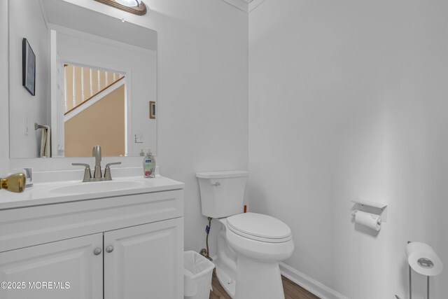 bathroom with toilet, wood finished floors, vanity, and baseboards