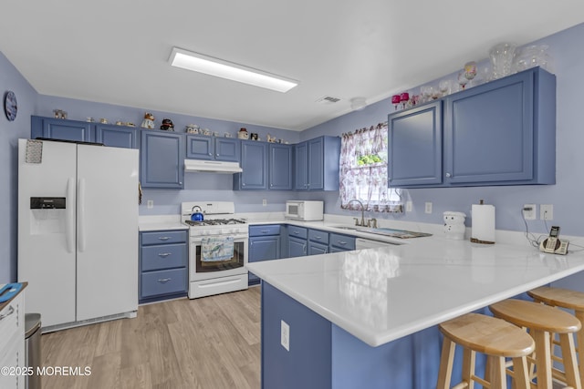 kitchen featuring white appliances, blue cabinets, under cabinet range hood, a peninsula, and a kitchen breakfast bar