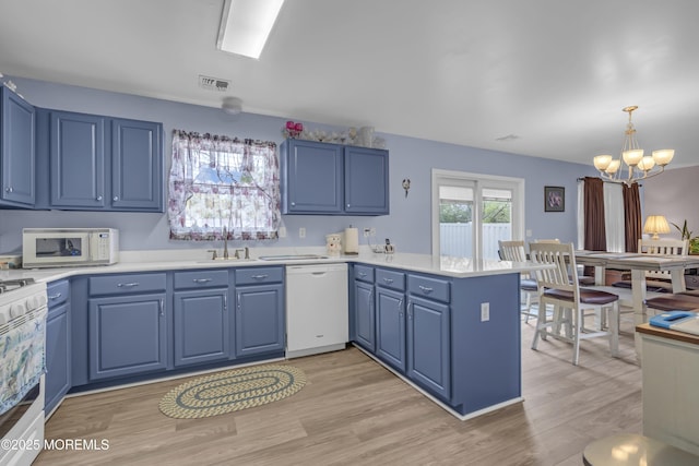 kitchen with white appliances, blue cabinetry, a chandelier, and a peninsula