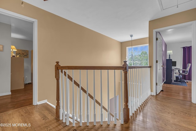 corridor featuring an upstairs landing, wood finished floors, baseboards, and attic access
