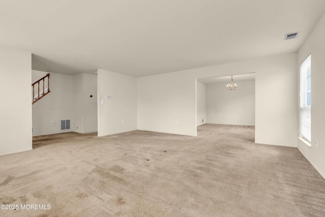 unfurnished living room with light colored carpet, healthy amount of natural light, a chandelier, and stairs