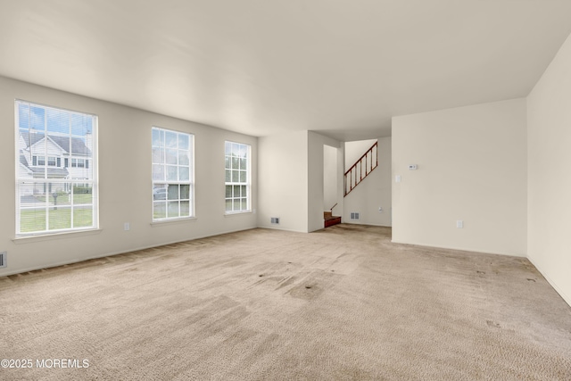 unfurnished living room featuring carpet and stairway