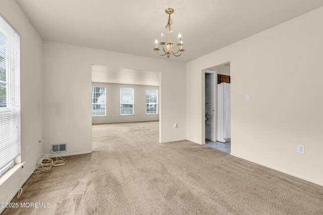 carpeted empty room featuring a chandelier, healthy amount of natural light, and baseboards