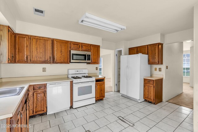 kitchen featuring white appliances, brown cabinets, light countertops, and a sink