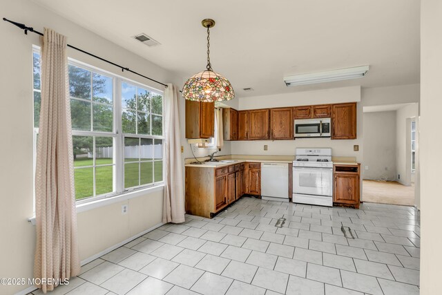 kitchen featuring white appliances, brown cabinets, light countertops, and healthy amount of natural light