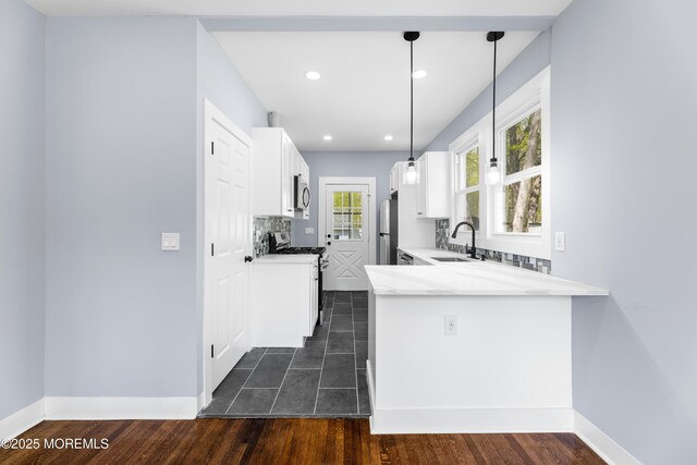 kitchen with stainless steel appliances, a sink, white cabinets, light countertops, and baseboards