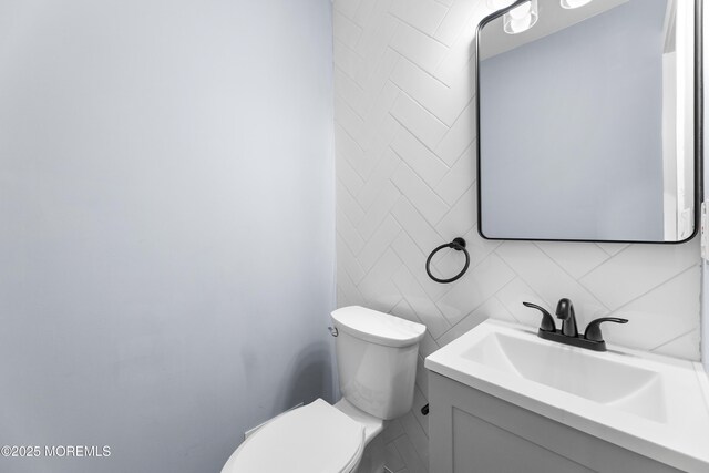 half bathroom with decorative backsplash, toilet, and vanity