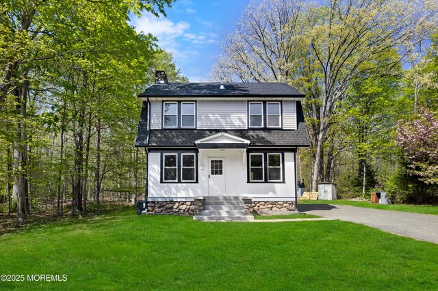 view of front of property featuring a chimney, a front lawn, roof with shingles, and asphalt driveway