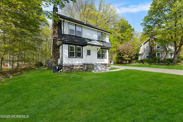 view of front of property with a chimney, a front yard, central AC, and a shingled roof