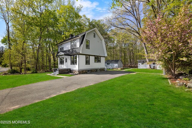 colonial inspired home with a gambrel roof, asphalt driveway, a front lawn, and a chimney