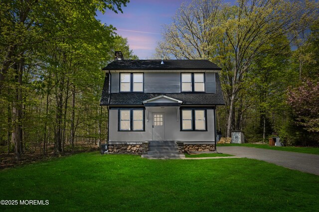 view of front of house with a chimney, a yard, roof with shingles, and driveway