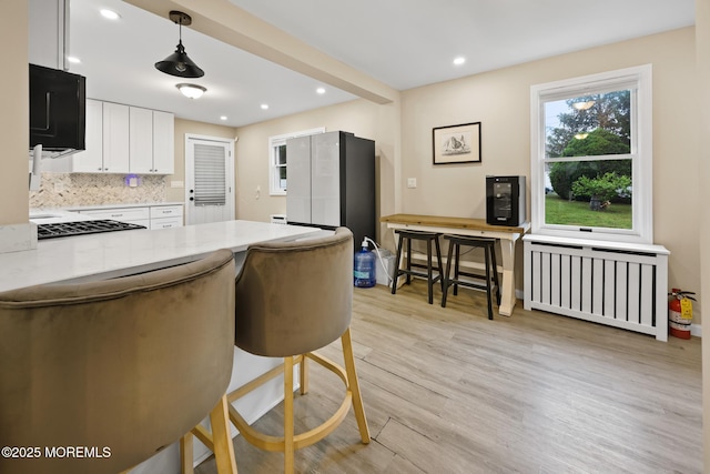kitchen featuring a peninsula, white cabinetry, light wood-style floors, decorative backsplash, and radiator heating unit