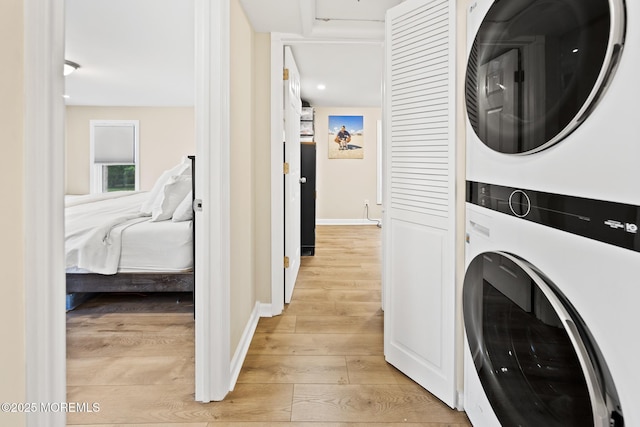 clothes washing area with stacked washer and clothes dryer, laundry area, light wood-style floors, and baseboards