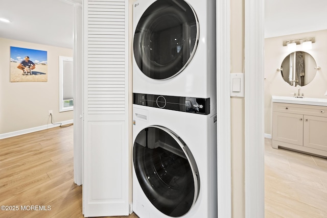 clothes washing area with stacked washer / dryer, laundry area, light wood-style flooring, and baseboards