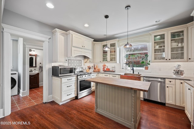 kitchen with a sink, washer / clothes dryer, stainless steel appliances, tasteful backsplash, and butcher block counters