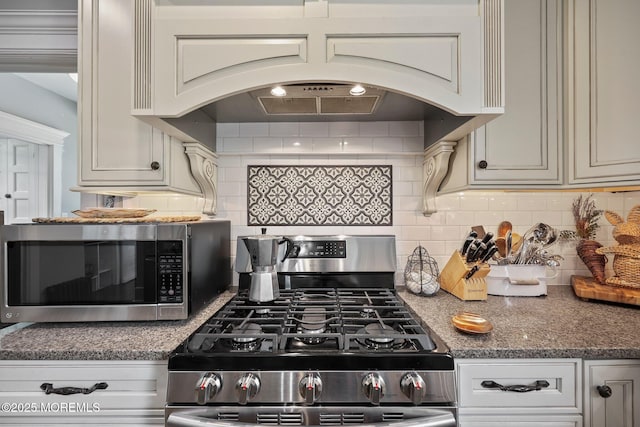 kitchen featuring premium range hood, stainless steel appliances, backsplash, and dark stone counters