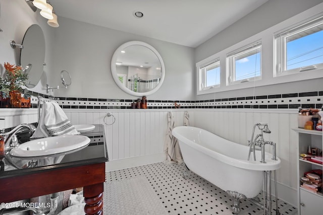 bathroom with wainscoting, tile walls, a soaking tub, and a sink