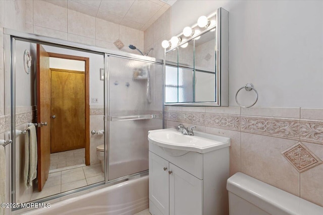 full bath with toilet, tile walls, bath / shower combo with glass door, and vanity