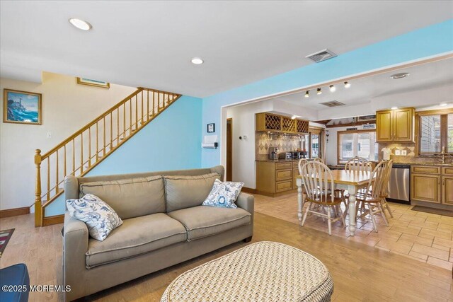 living room featuring a bar, stairs, light wood-style floors, recessed lighting, and baseboards