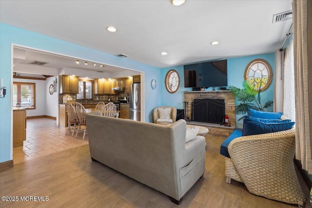 living room featuring a fireplace with raised hearth, recessed lighting, baseboards, and light wood-type flooring