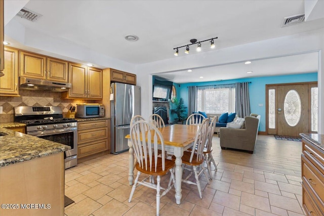 kitchen featuring appliances with stainless steel finishes, under cabinet range hood, backsplash, dark stone countertops, and open floor plan