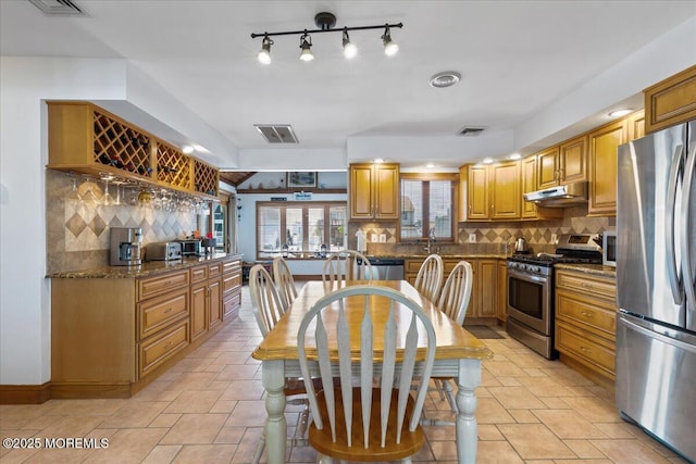 kitchen with stainless steel appliances, under cabinet range hood, tasteful backsplash, dark stone countertops, and a sink