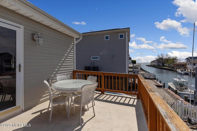wooden deck with a water view, outdoor dining space, and cooling unit