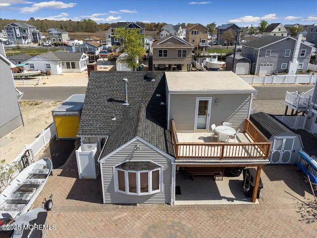 back of house featuring a residential view, a storage shed, roof with shingles, an outdoor structure, and a fenced backyard