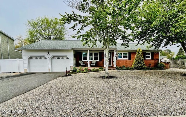 single story home with a porch, an attached garage, fence, driveway, and brick siding