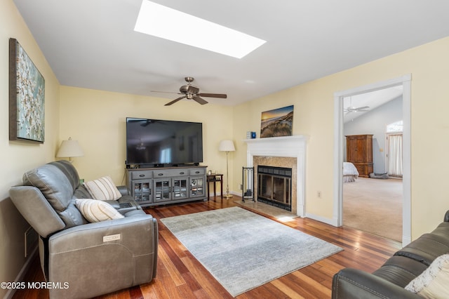 living area with a ceiling fan, a skylight, wood finished floors, and a glass covered fireplace