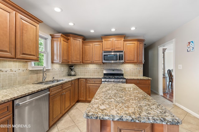 kitchen featuring stainless steel appliances, a sink, light stone counters, brown cabinets, and recessed lighting