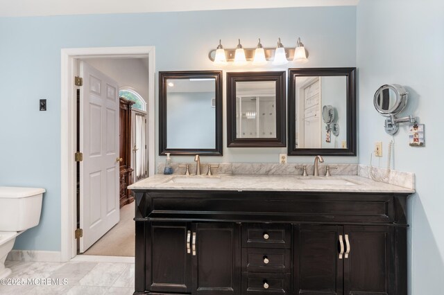 bathroom with baseboards, toilet, double vanity, and marble look tile flooring