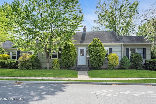view of front of property with entry steps, a chimney, and a front yard