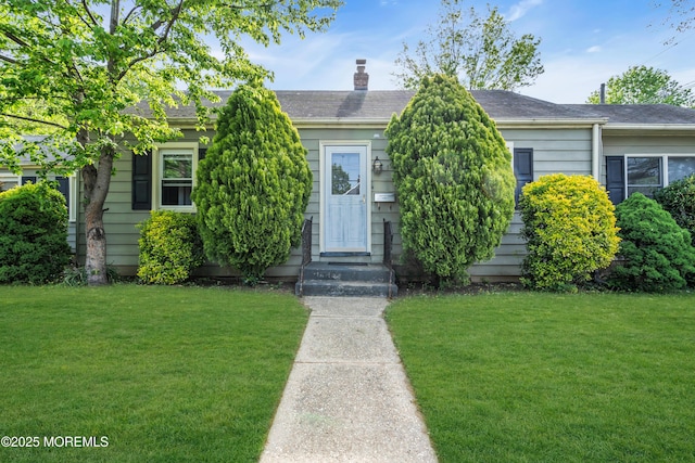 view of property hidden behind natural elements with a front lawn and a chimney