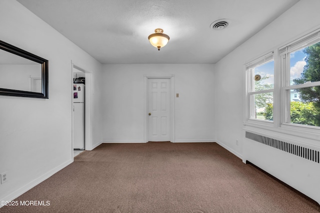 spare room featuring carpet flooring, radiator, and baseboards
