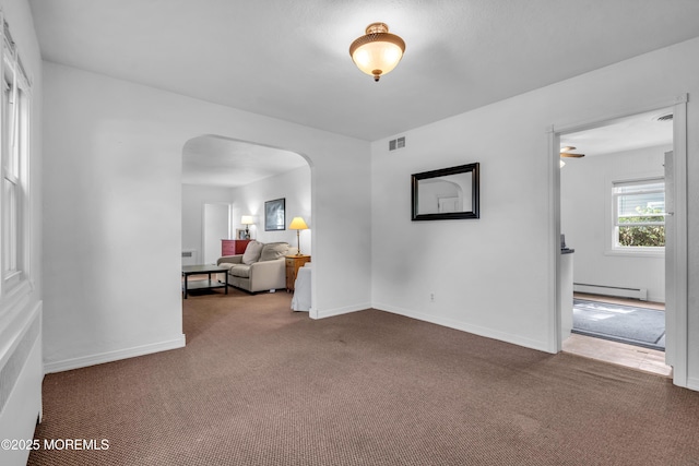 carpeted spare room featuring baseboard heating, arched walkways, and baseboards