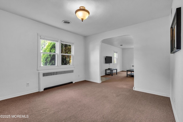 empty room featuring radiator, arched walkways, carpet, and baseboards