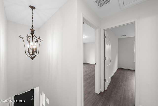 corridor featuring dark wood-style flooring, a chandelier, and baseboards
