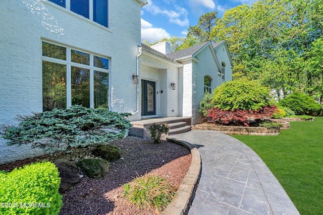 view of exterior entry featuring a yard and brick siding