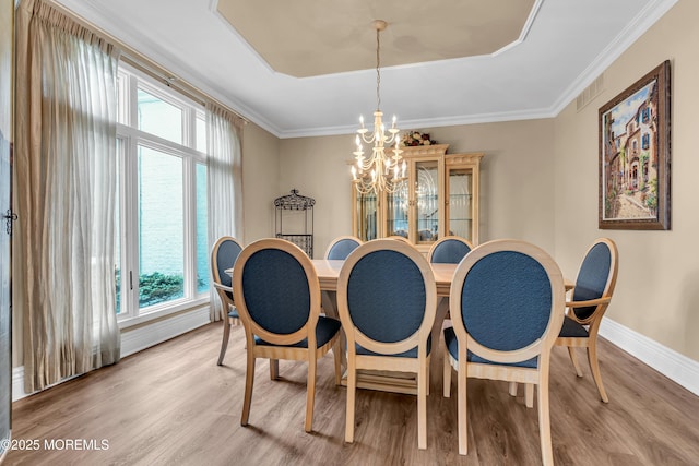 dining area featuring light wood-style floors, a chandelier, crown molding, baseboards, and a raised ceiling