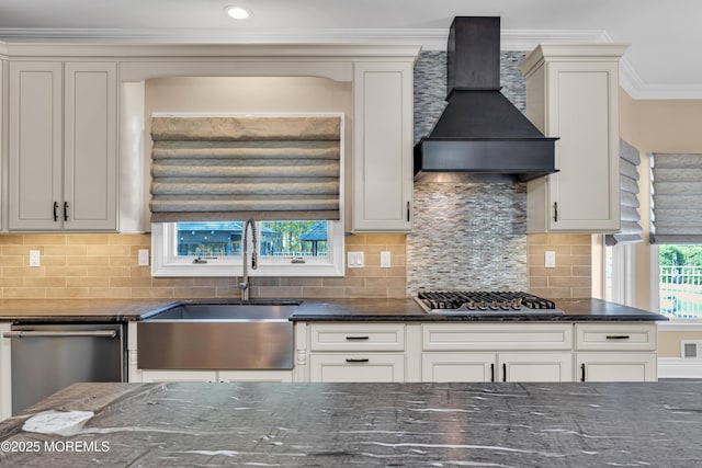 kitchen with wall chimney exhaust hood, appliances with stainless steel finishes, a sink, dark stone countertops, and crown molding