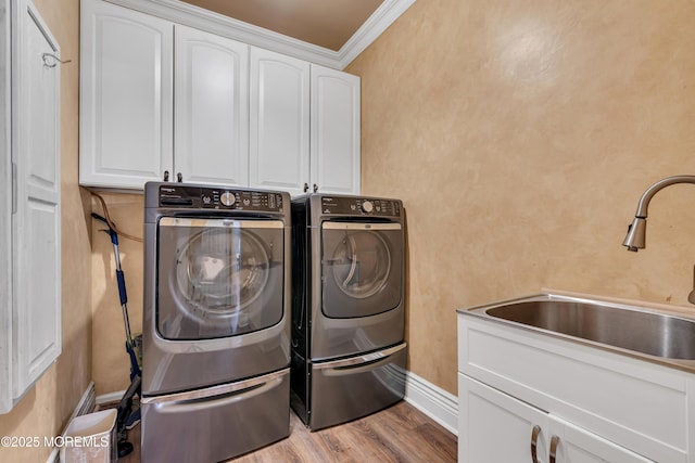 washroom featuring cabinet space, washing machine and clothes dryer, wood finished floors, crown molding, and baseboards