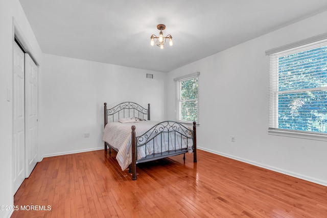 bedroom featuring light wood-type flooring, a chandelier, a closet, and baseboards