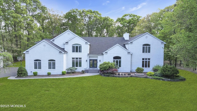 view of front of house featuring a front yard, a chimney, roof with shingles, french doors, and view of wooded area