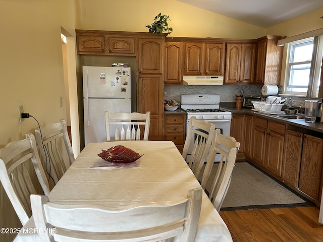 kitchen with white appliances, under cabinet range hood, dark wood-style floors, brown cabinets, and lofted ceiling