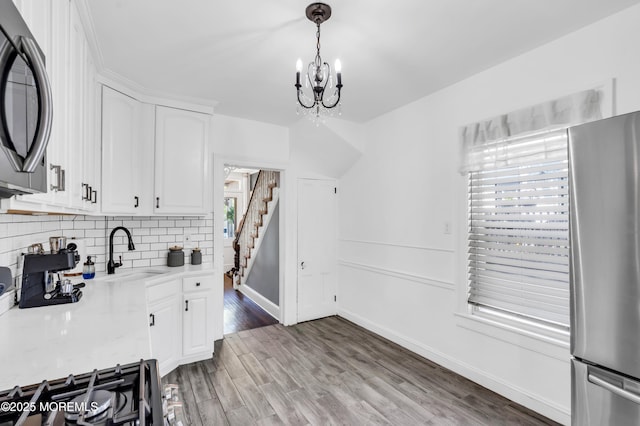 kitchen featuring freestanding refrigerator, a sink, light countertops, white cabinets, and a chandelier