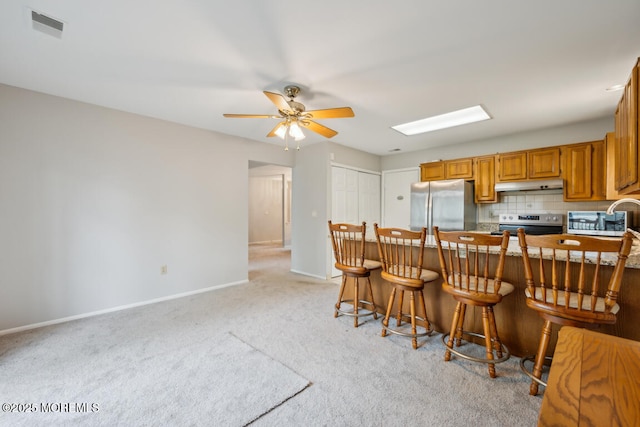 119 Morning Glory, Whiting, NJ 08759 - kitchen featuring appliances with stainless steel finishes, under cabinet range hood, light carpet, a ceiling fan, and a breakfast bar