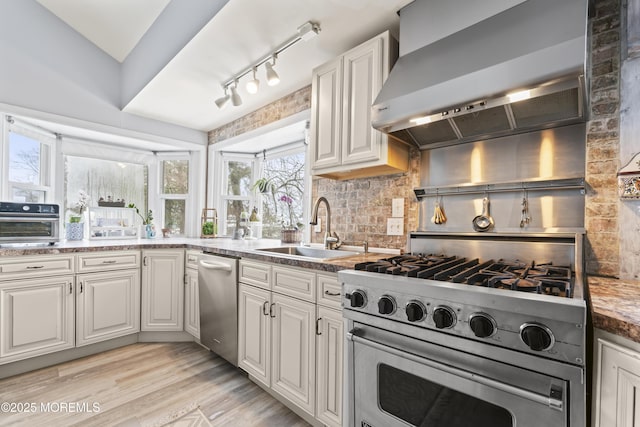 kitchen featuring wall chimney exhaust hood, stainless steel dishwasher, a sink, and white cabinetry