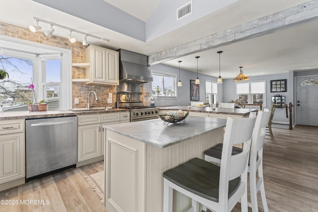 kitchen with appliances with stainless steel finishes, a sink, track lighting, light wood-style flooring, and a breakfast bar
