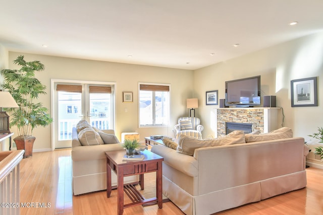 living room with a stone fireplace, light wood-style flooring, recessed lighting, and baseboards